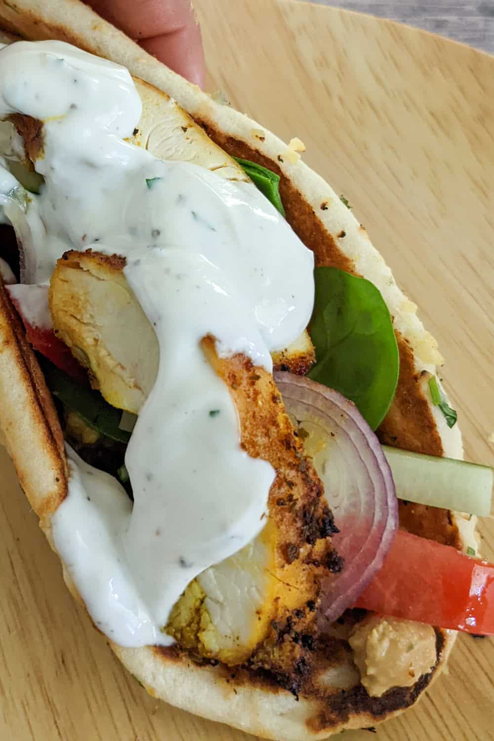 zhug feta hummus chicken wrap on a bamboo plate and folded in hand